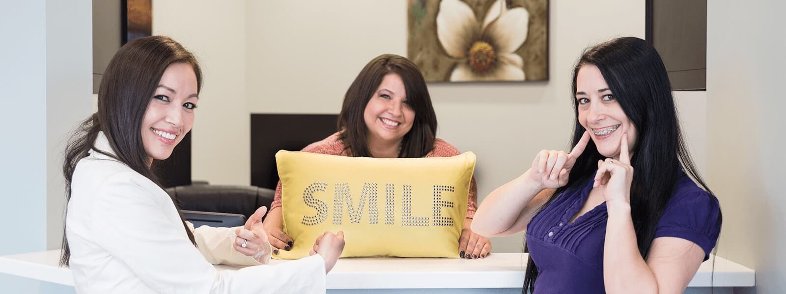 Dr. Tran and two team members smiling and holding up a yellow pillow that says Smile