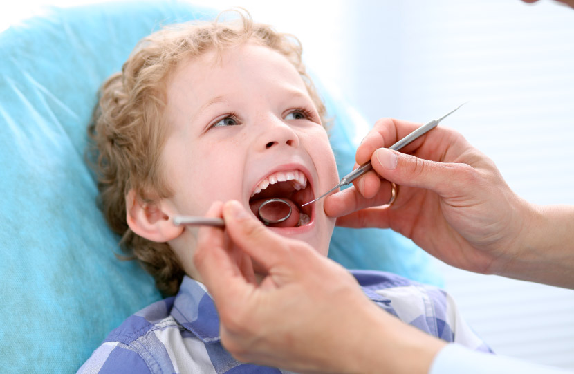 Blonde curly-haired boy sits happily in the dental chair at his first dental visit