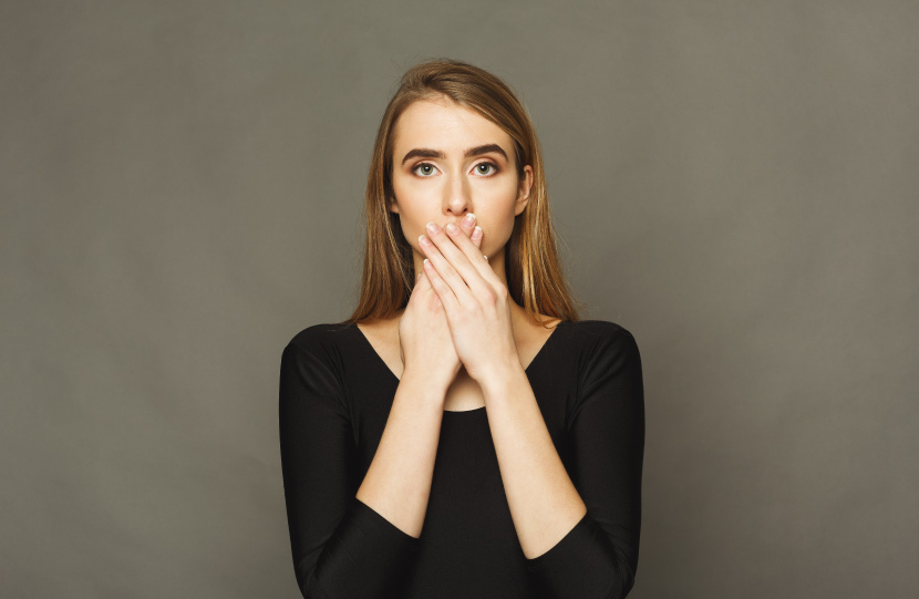 Blonde woman wearing a black shirt covers her mouth due to embarrassing white spots on her gums