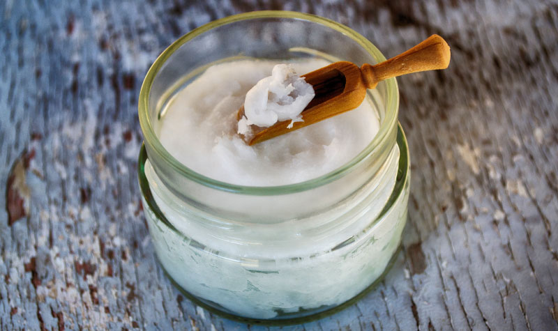 Closeup of a clear container of white coconut oil used for oil pulling and a brown scoop