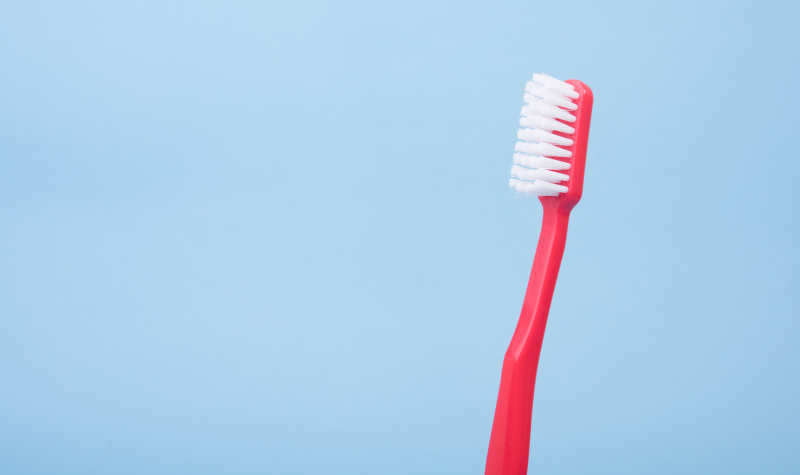 Closeup of a red toothbrush with white soft bristles against a blue background