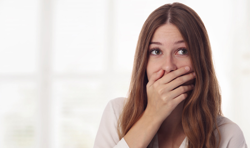 Brunette woman covers her mouth due to bad breath from an untreated cavity