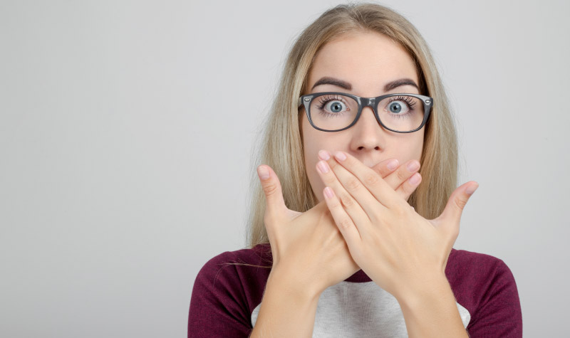 girl with glasses covering her mouth with both hands to hide tooth decay