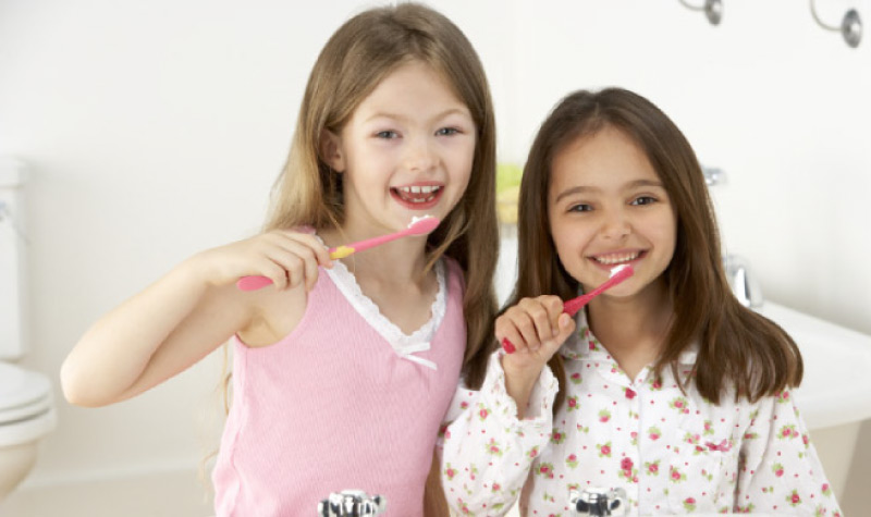 two young girls brushing their teeth together