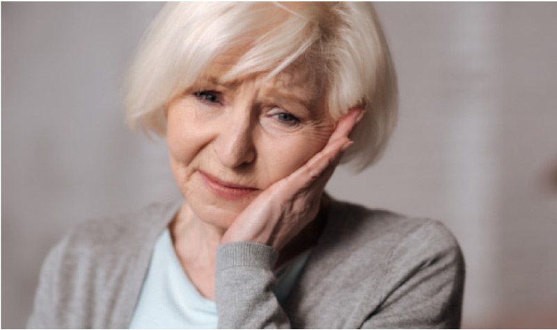 senior woman holds her jaw in pain from a missing tooth