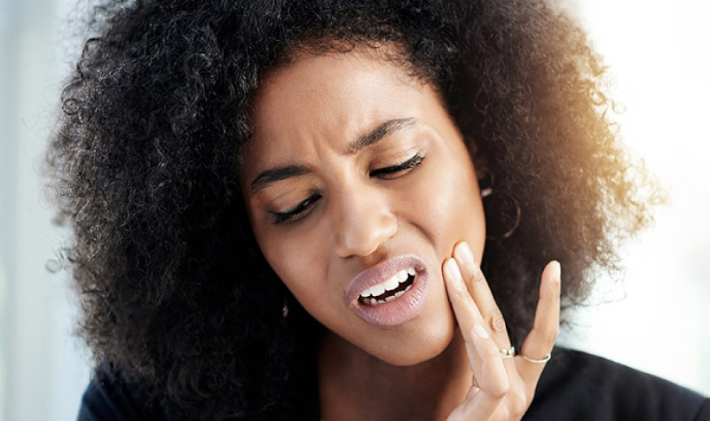 Attractive young black woman with a pained look on her face and fingers on her cheek indicating tooth pain