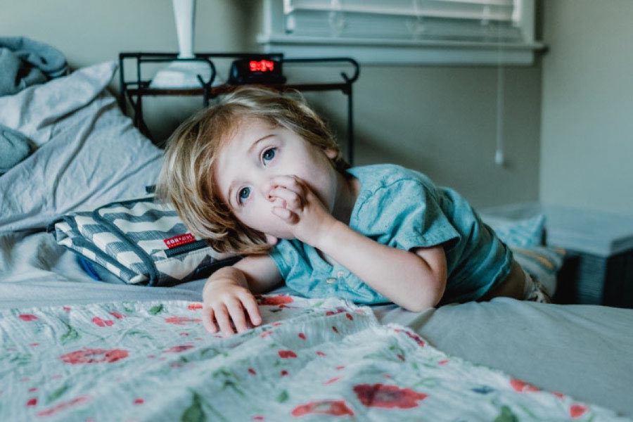 young boy leaning on a bed sucking his thumb