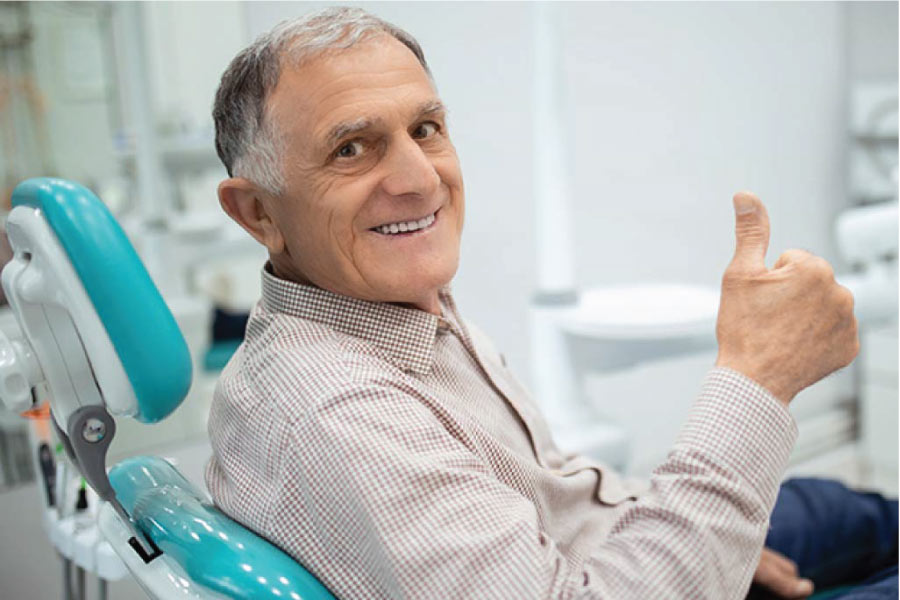 senior man sitting in the dentist chair gives a thumbs up for high quality dentures