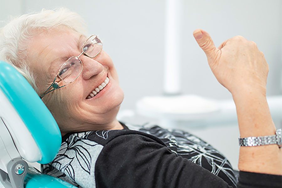 senior woman in the dentist chair smiles and gives a thumbs up after using her dental insurance before it expires