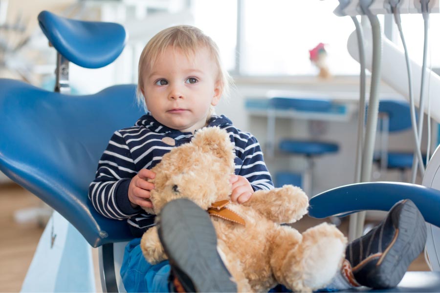 young boy sits in the dentist chair with a teddy bear