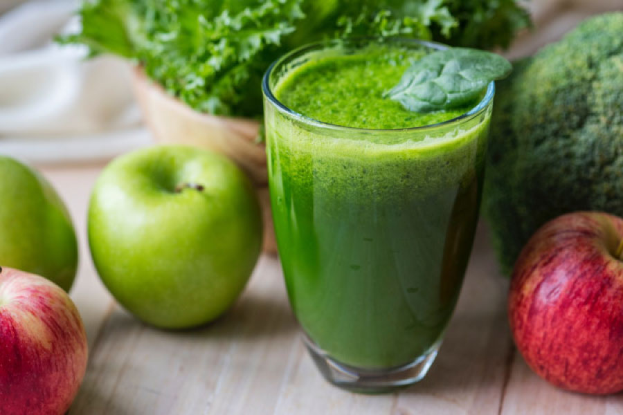 green smoothie in a glass next to apples