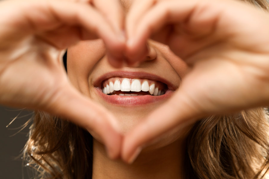 woman makes a hand heart in front of her smile