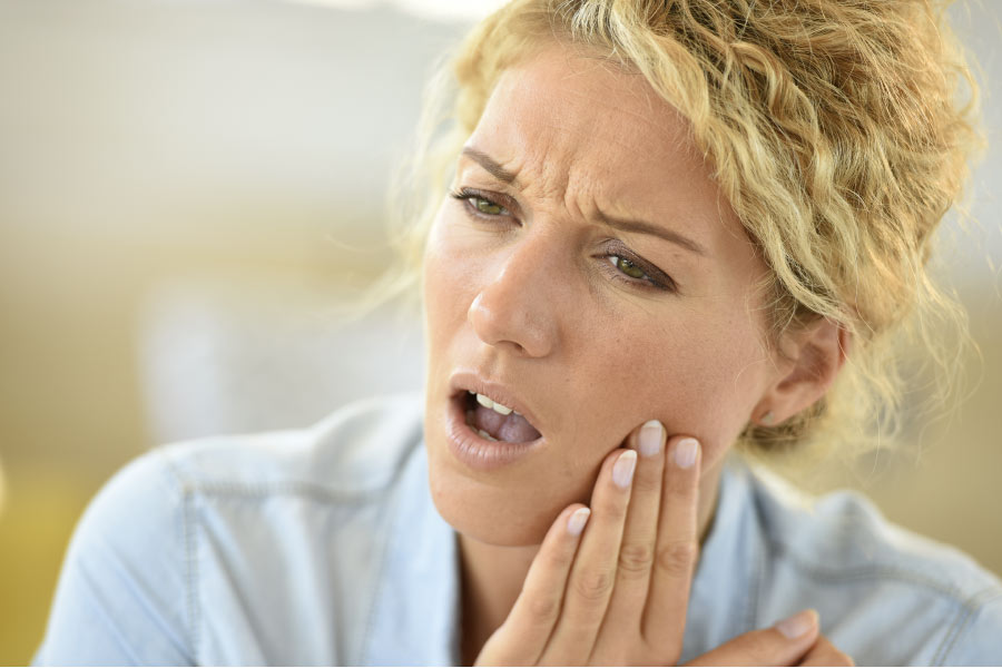 woman holds her cheek and grimaces with tooth pain